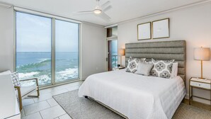 Quarto com cama grande, ventoinha no teto, vista para o oceano e mesa de cabeceira com abajur.