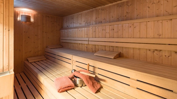 Uma sauna com bancos de madeira e um assento, uma toalha e um balde de metal.