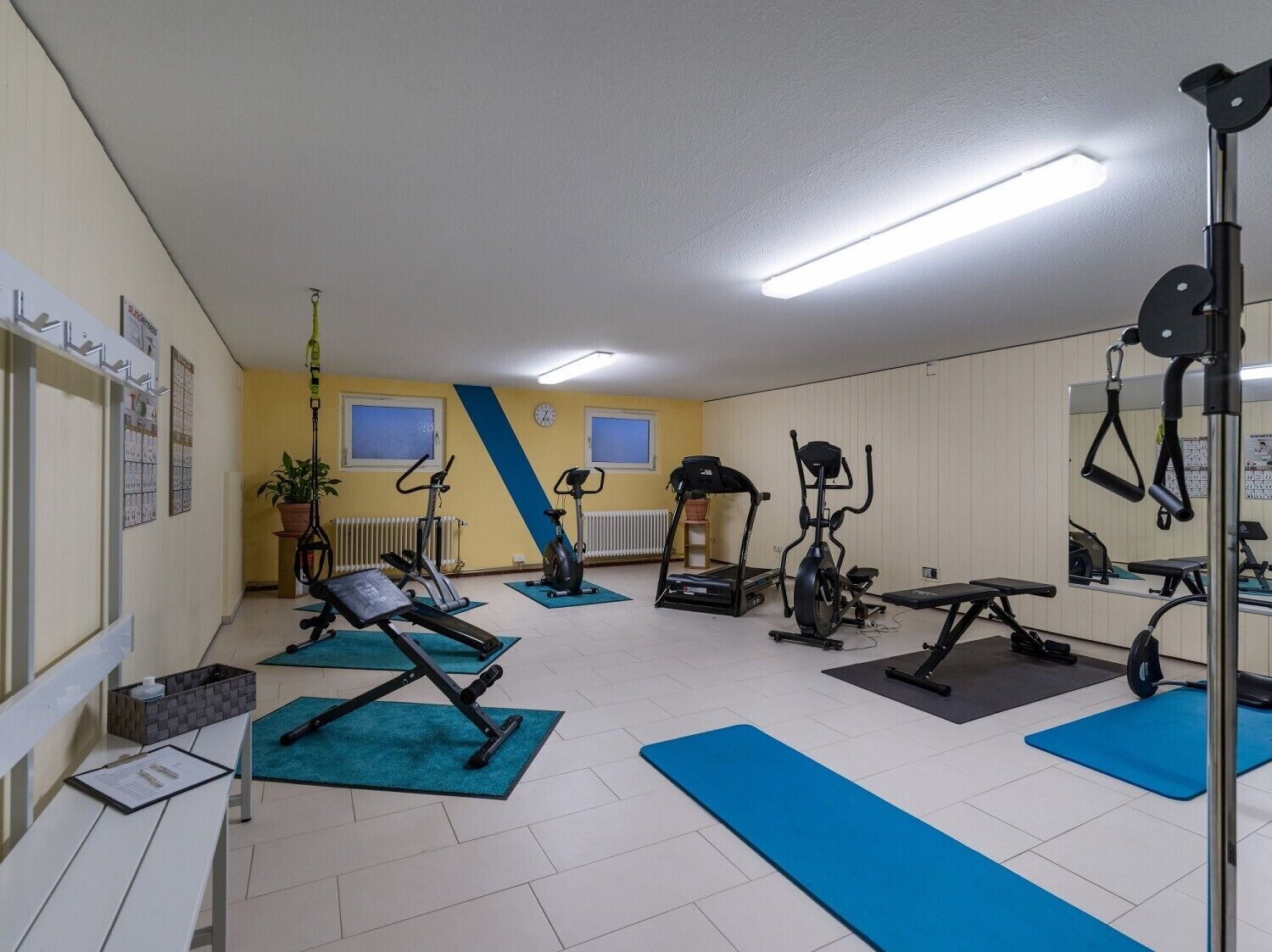 Une salle de sport équipée de matériel d’exercice, avec des tapis bleus et un sol blanc.
