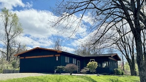 A two-story house with a dark exterior and a sloped roof, surrounded by a well-maintained lawn and trees. - Cocktail Cove 4 bedroom 2 bath by Jamestown Marina (Jamestown)