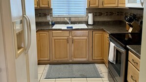 A kitchen with wooden cabinets, a stainless steel refrigerator, a microwave, and an oven. There is a window with blinds and a sign above the sink. - Cocktail Cove 4 bedroom 2 bath by Jamestown Marina (Jamestown)