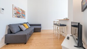 A modern living room with a grey sectional sofa, a dining table with chairs, a flat-screen TV, and a painting on the wall.