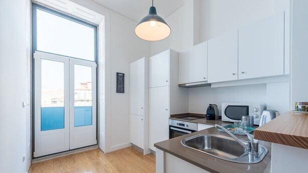 A modern kitchen with white cabinets, a stainless steel sink, a kettle, a microwave, and a toaster.