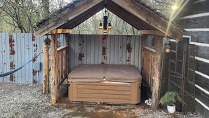 Un bain à remous en bois rustique, doté d’un toit incliné, entouré d’une clôture en métal et d’un mur en tôle ondulée.