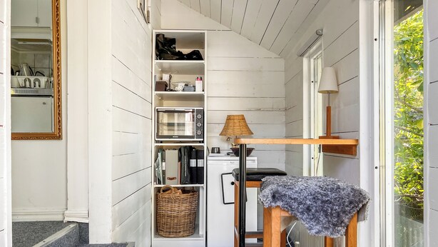 A compact kitchen with white wooden walls, a microwave, a wicker basket, and a small stool with a gray cloth. - Small cottage close to Stockholm City  (Saltsjö-boo)