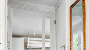 A narrow hallway leading to a bedroom with a bunk bed, a white door with a gold frame, and a mirror on the right wall. - Small cottage close to Stockholm City  (Saltsjö-boo)