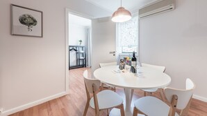Et moderne spiseområde med et rundt hvidt bord, træstole, en hængende lampe og et indrammet kunstværk på væggen.