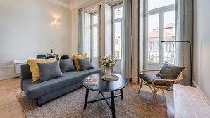 A modern living room with a grey sofa, a round coffee table, and a wicker chair. - GuestReady - Visconde Mezzanine (Porto)