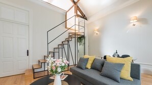 A modern living room with a grey sofa, black coffee table, and a staircase with a geometric design. - GuestReady - Visconde Mezzanine (Porto)