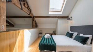 A bedroom with a skylight, a bed with pillows, a chair, and a small table. - GuestReady - Visconde Mezzanine (Porto)