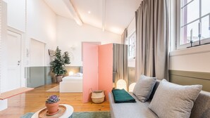 En moderne stue med en sofa, et lille bord med en potteplante, en seng med et natbord, og en lyserød rumdeler.