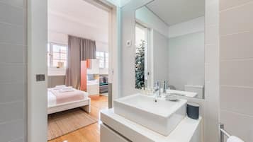A modern bathroom with a large sink, mirror, and a view of a bedroom with a bed and a window.
