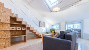 A modern loft with exposed wooden beams, a staircase, a grey sofa, and a skylight. - GuestReady - Mezzanine at the Bridge (Porto)