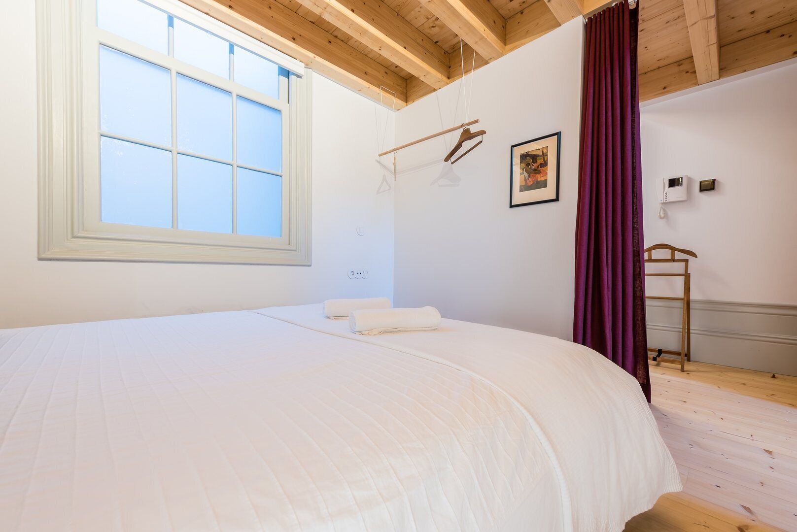 Un dormitorio con una cama grande, una ventana, techo de madera y aire acondicionado instalado en la pared.