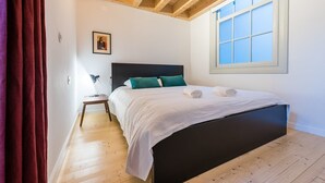 A bedroom with a bed, a nightstand, a window, and wooden beams on the ceiling. - GuestReady - Mezzanine at the Bridge (Porto)