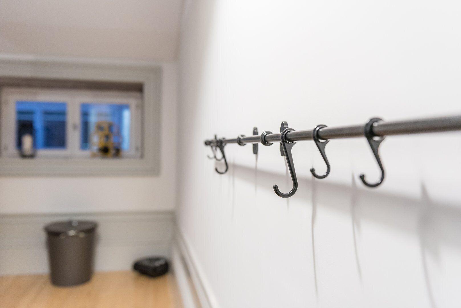 A metal hook bar on a white wall with a window in the background.