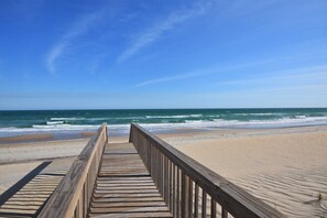 A wooden boardwalk leading to a beach with waves and a clear sky.