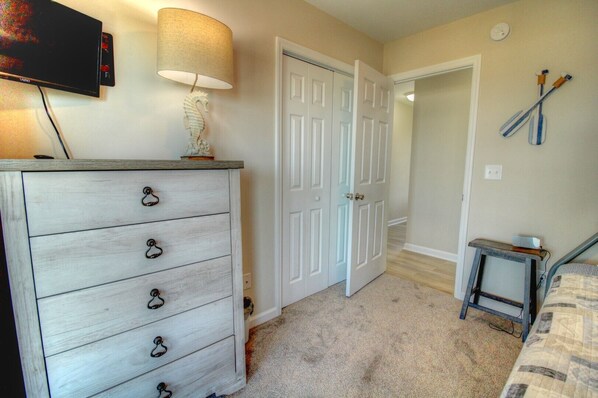 A bedroom with a dresser, a lamp, a bed, and a TV.