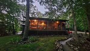 Eine Holzhütte mit einer Holzterrasse, umgeben von Bäumen und einem kleinen Bach.