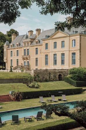 Un grand bâtiment de style classique, doté d’une piscine et de chaises longues.