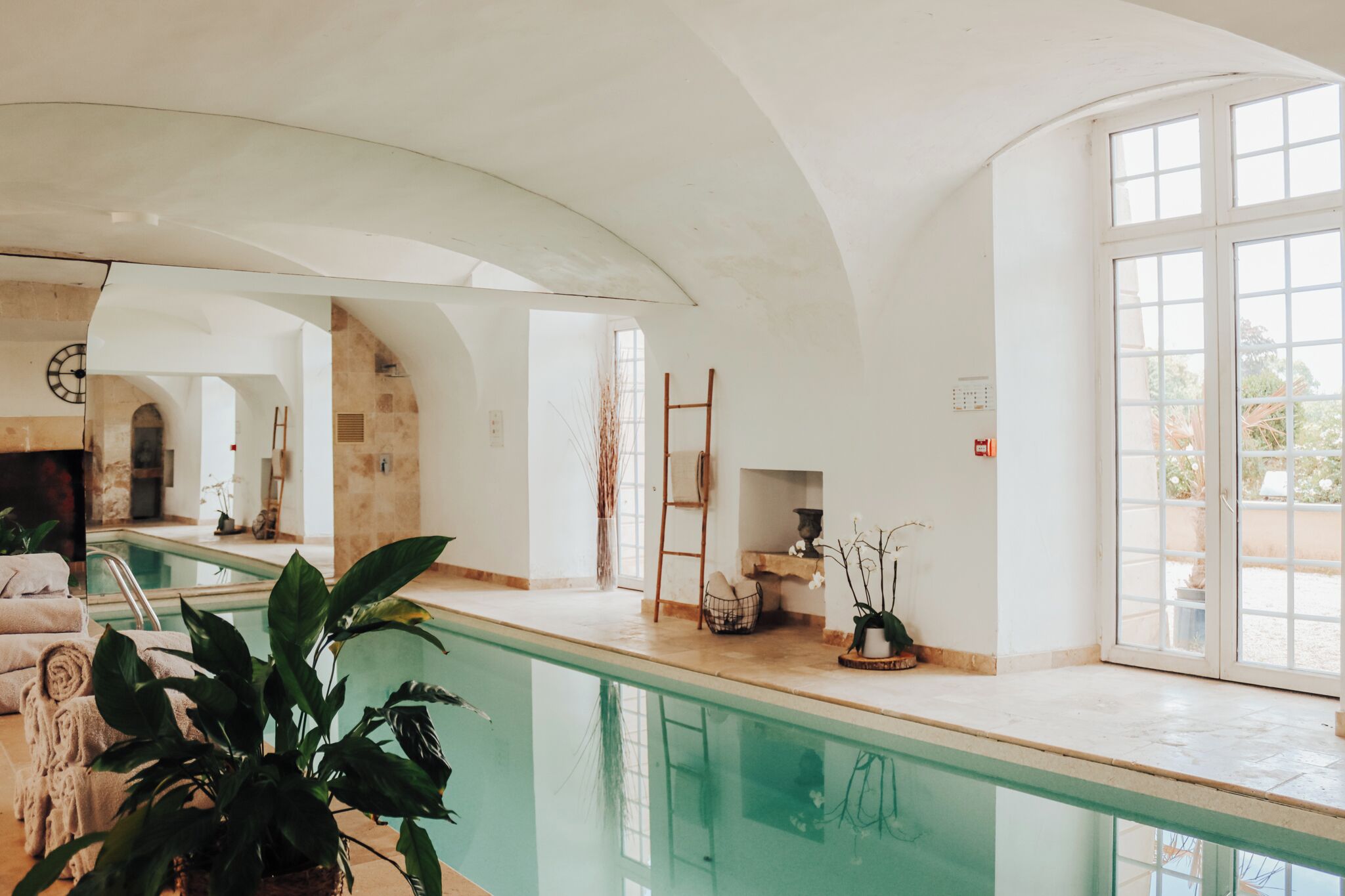 A spacious indoor swimming pool area with a clear view of the pool, a lounge area with seating, and a stone wall.