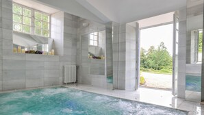 A spacious indoor swimming pool with clear views of the outdoors, a large mirror, and a window with a view of greenery. - Château with Spa, Golf, Tennis, Basket, swimming pools, gardens.  (Villers-Bocage)