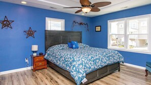 A bedroom with a bed, a nightstand, a wooden floor, a ceiling fan, and a window with a view.