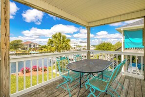 A covered outdoor area with a table and chairs, a view of a body of water, and a distant building. - Mama's Pride - 3BR Home on the Canal - Boat Dock & Sound Views! (Surf City)