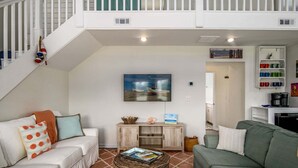 A living room with a white staircase, a painting of a boat, a coffee machine, and a bookshelf. - Dream Weaver: Spacious 4BR home in Holden Beach, perfect for family getaways! (Holden Beach)