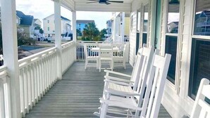 A covered porch with white rocking chairs and a ceiling fan. - Dream Weaver: Spacious 4BR home in Holden Beach, perfect for family getaways! (Holden Beach)