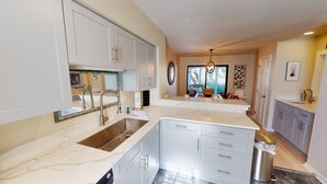 Une cuisine moderne avec des meubles blancs, un plan de travail en marbre et un grand îlot central doté d’un évier.