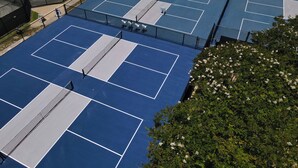 Vue aérienne d’un complexe de courts de tennis comprenant plusieurs terrains, des zones d’assise et une clôture périphérique.
