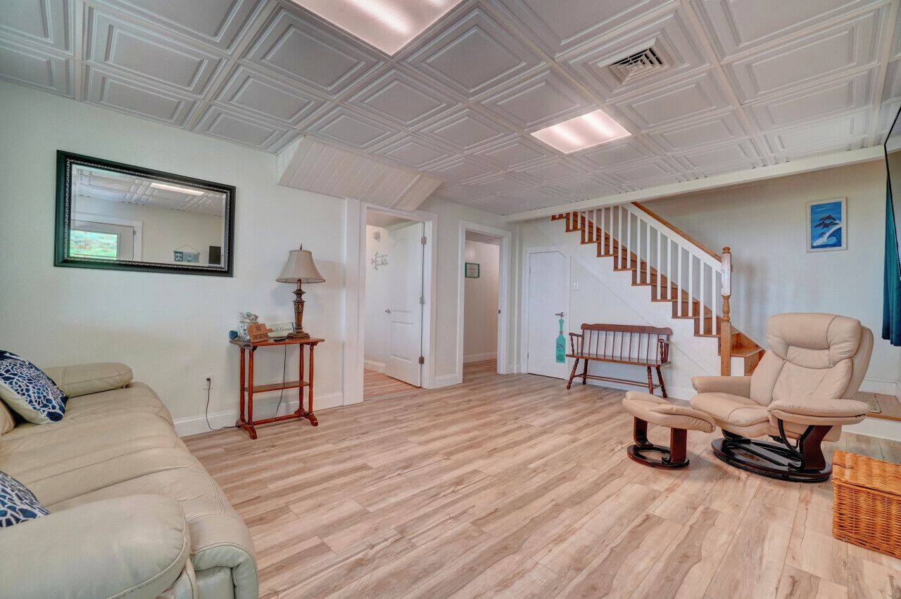 A spacious living room with a wooden floor, a beige sofa, a recliner, a mirror, and a staircase leading upstairs.