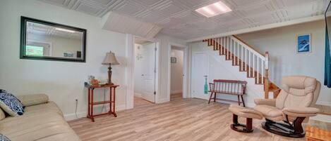 A spacious living room with a wooden floor, a beige sofa, a recliner, a mirror, and a staircase leading upstairs.