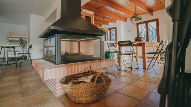 Una habitación acogedora con chimenea, vigas de madera y una zona de comedor con sillas y mesa.