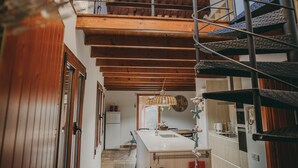 Una cocina con techo de madera, una isla central y una escalera que lleva a un nivel superior.
