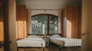 Una habitación con dos camas, paredes de madera, un ventanal con cortinas y vistas a árboles.