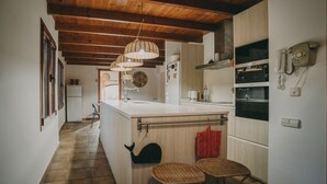 Una cocina con vigas de madera, una isla central, una lámpara colgante y un reloj en la pared.