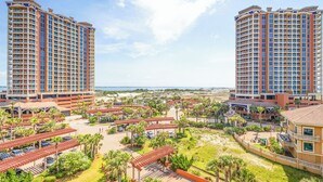 Un hotel de gran altura con múltiples balcones, un área de estacionamiento y vista al mar.