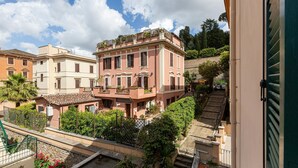 Un edificio de varios pisos con balcones, una escalera y abundante vegetación alrededor.