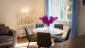 Un comedor moderno con una mesa redonda, cuatro sillas, un jarrón de flores moradas, una estantería blanca y un radiador.