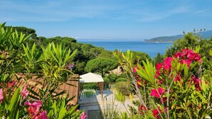 Um jardim com um pátio, um guarda-sol branco e vista para o mar.
