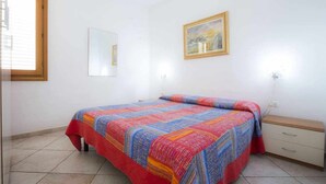 Ein Schlafzimmer mit einem Bett, einem Nachttisch, einer Kommode, einem Fenster und einem Wandbild.