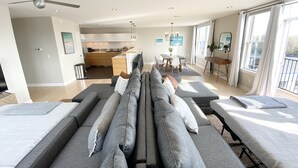 A modern living room with a sofa set, a dining area, and a kitchen in the background.