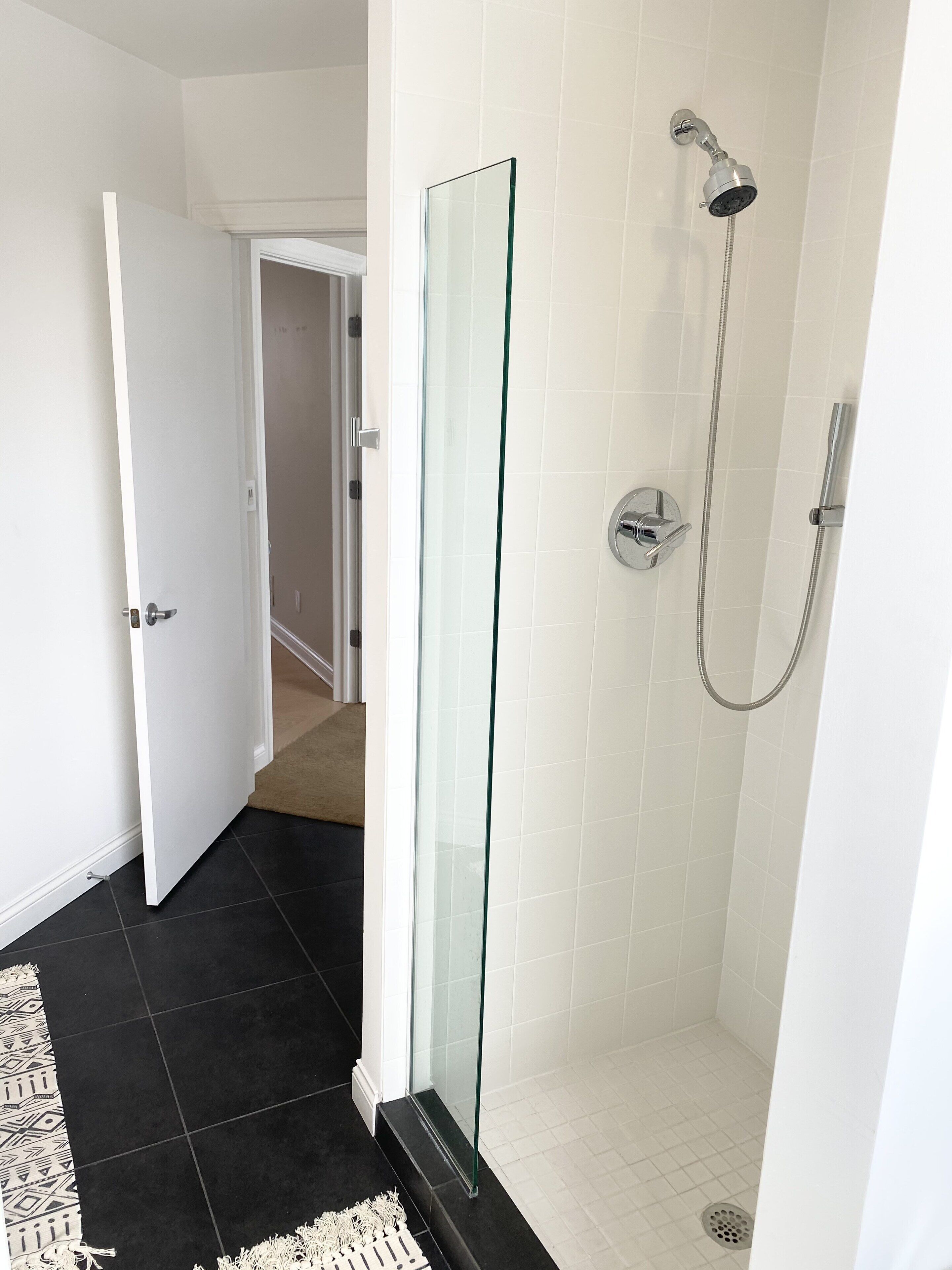 Une salle de bain moderne avec une douche à l’italienne en verre, des murs recouverts de carreaux blancs et un sol carrelé de noir.