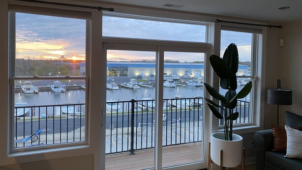 A room with large windows overlooking a marina and sunset.