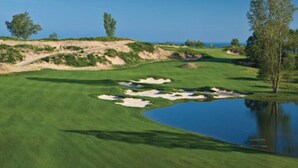 A golf course with sand bunkers, a pond, and trees.