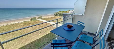 Un balcon avec une table et des chaises donnant sur une plage.