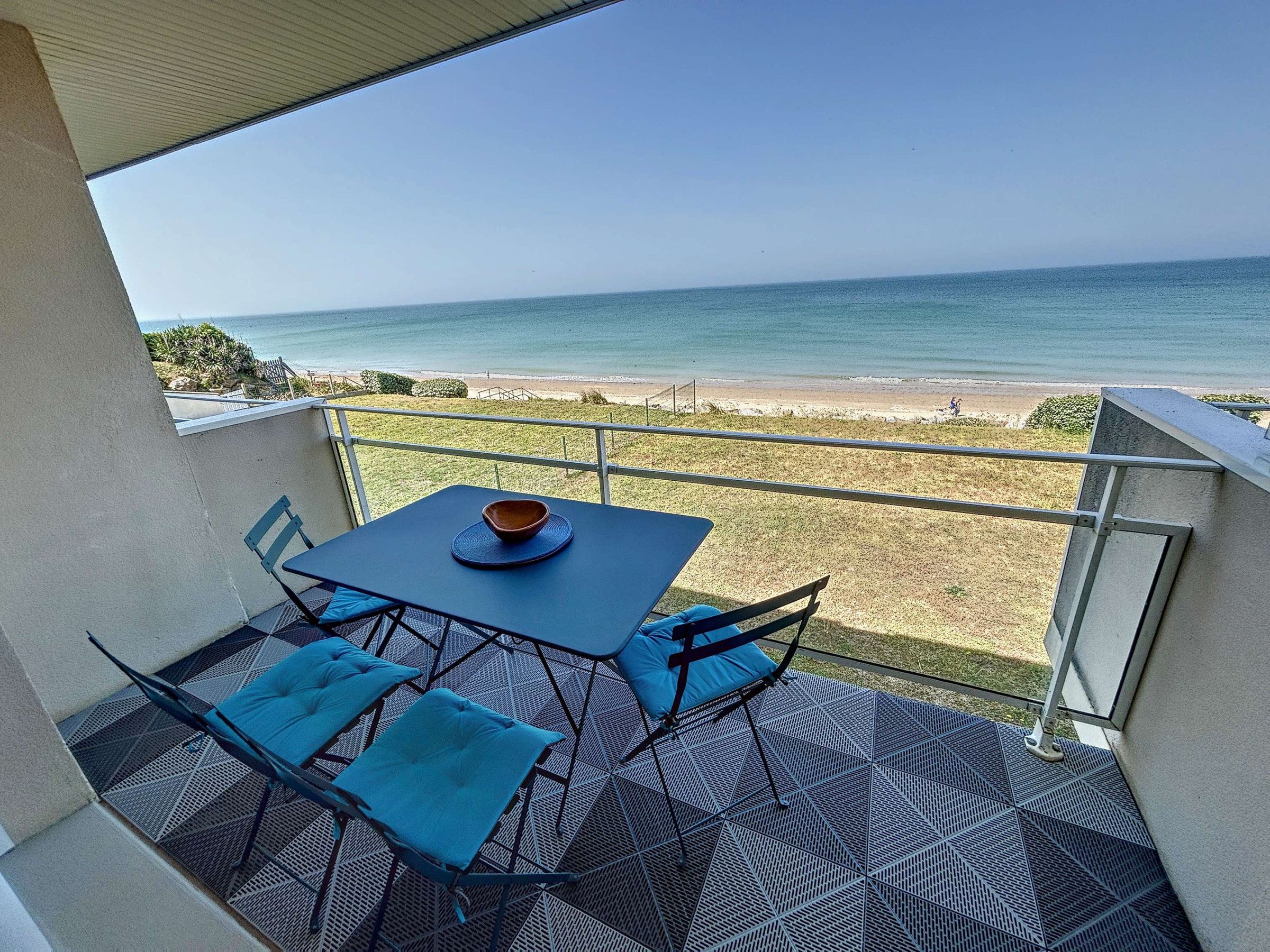 A balcony with a table and chairs, overlooking a beach and ocean.