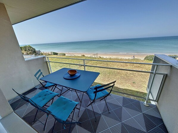 Un balcón con mesa y sillas, con vista a una playa y al océano.